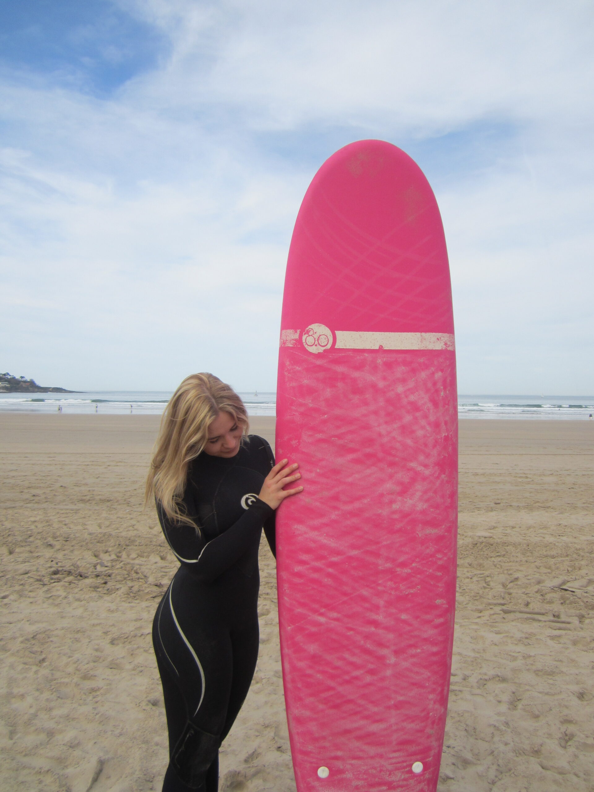 Noor naine hoiab roosa surfilauda Hendaye liivase ranna taustal