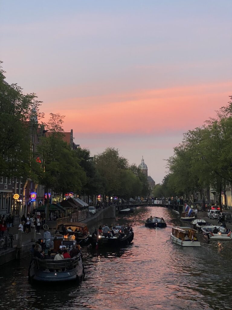 An Amsterdam canal with boats under a pink sunset